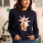 Woman wearing a navy blue sweater with a cat and star design, standing in front of a colorful wall with cat illustrations.