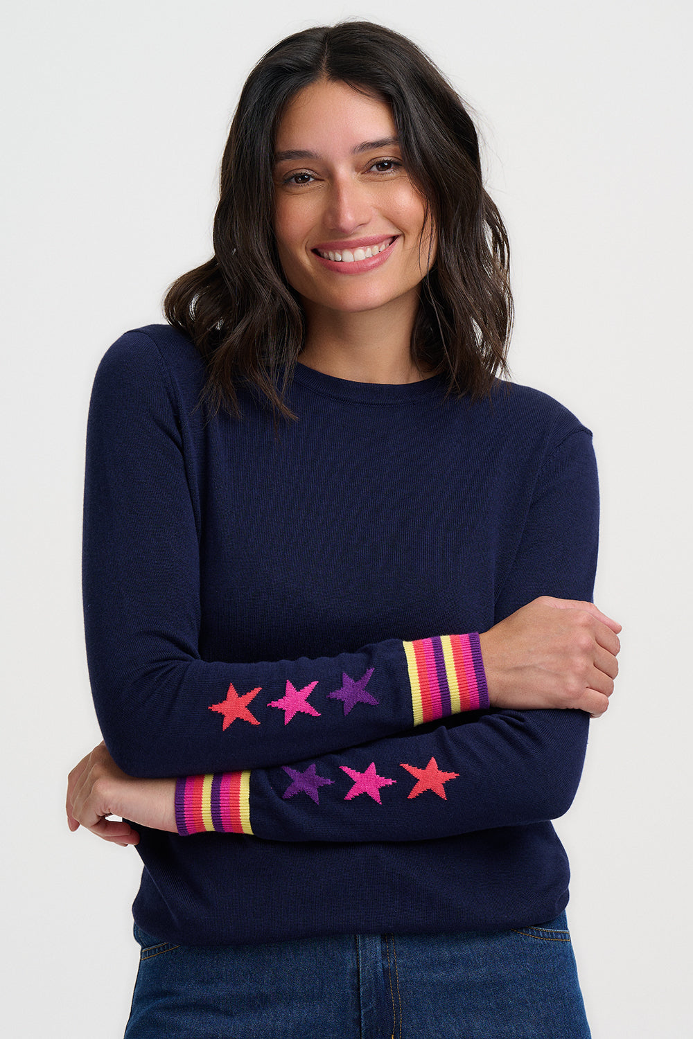 Woman wearing a navy sweater with colorful star patterns on sleeves against a white background