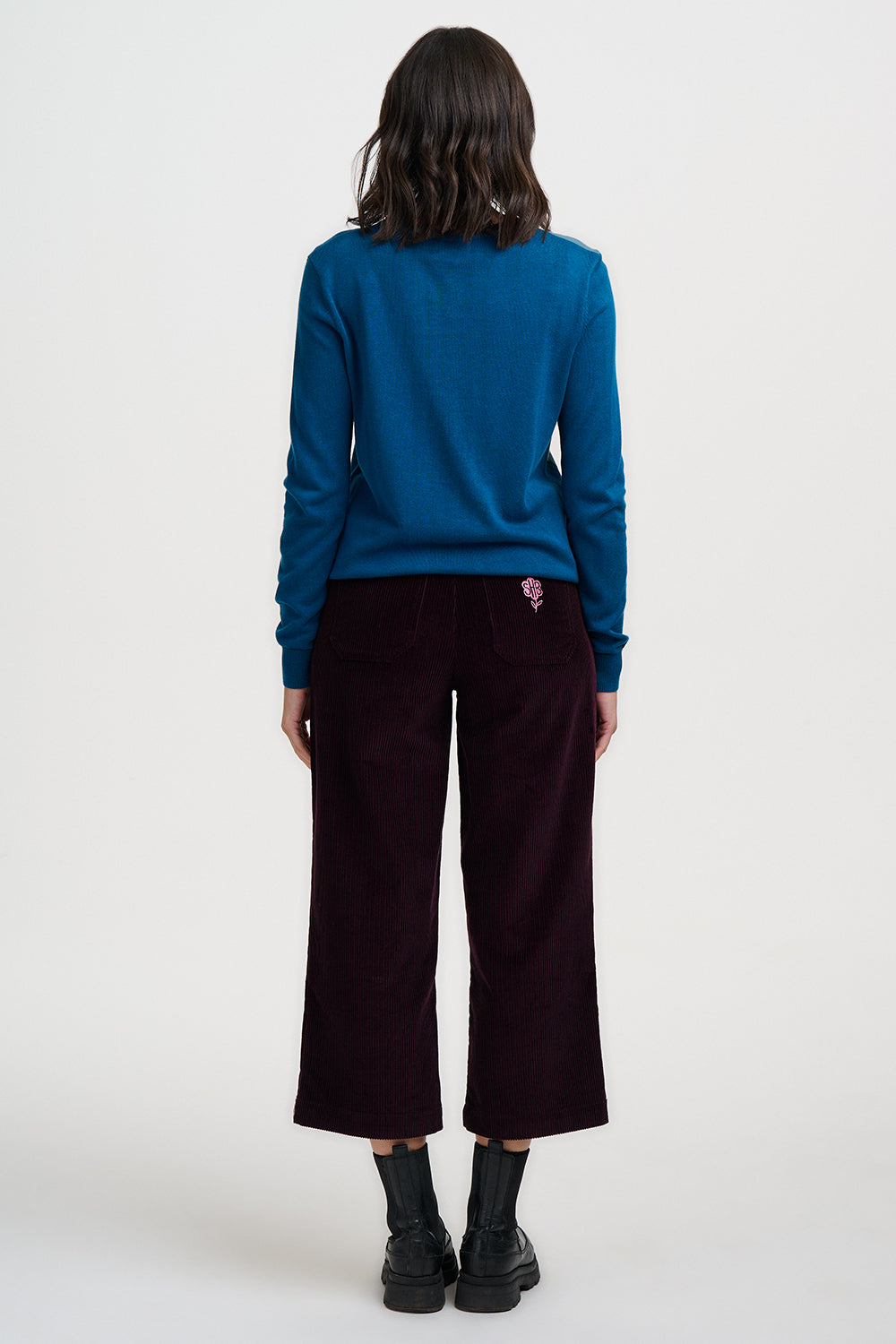 Person wearing a blue sweater and dark pants on a white background
