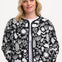 A woman wearing a monochrome quilted jacket with a floral folk print, featuring white leaves and flowers on a black base.