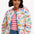 A woman wearing an off-white quilted jacket with a Tropical Hummingbird print, featuring front pockets and a round neckline.