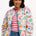 A woman wearing an off-white quilted jacket with a Tropical Hummingbird print, featuring front pockets and a round neckline.