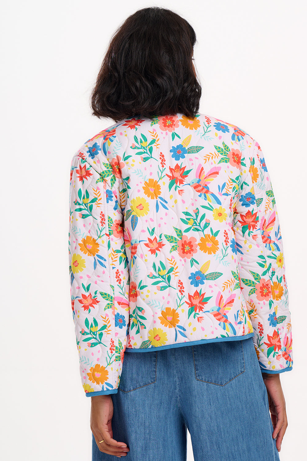 A woman wearing an off-white quilted jacket with a Tropical Hummingbird print, featuring front pockets and a round neckline.