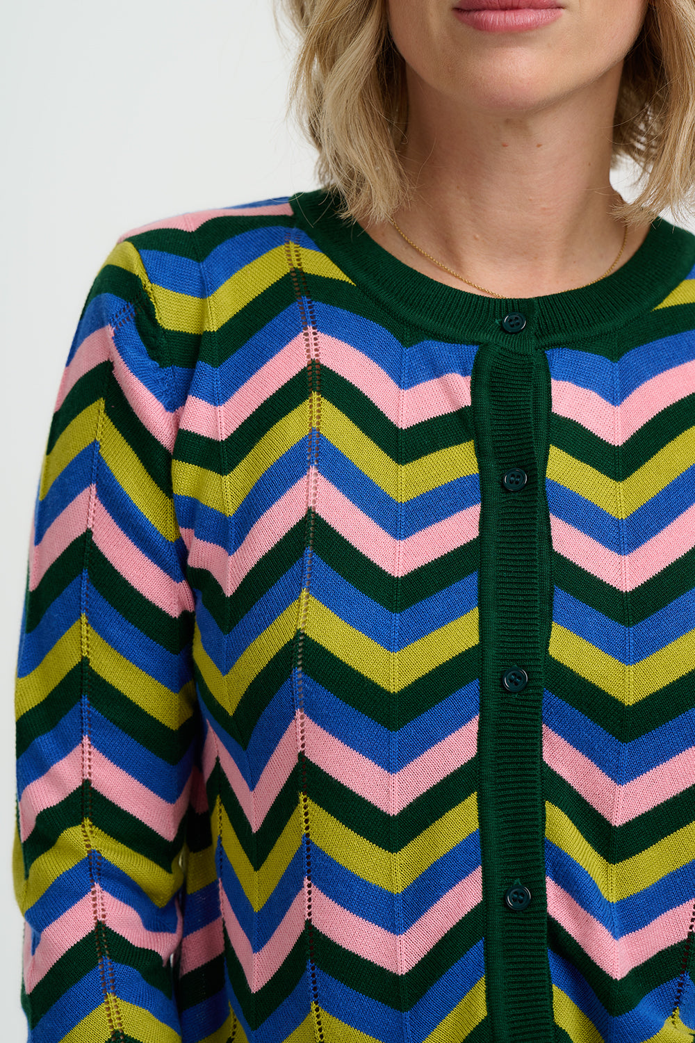 Woman wearing a colourful chevron-patterned sweater and blue jeans on a white background