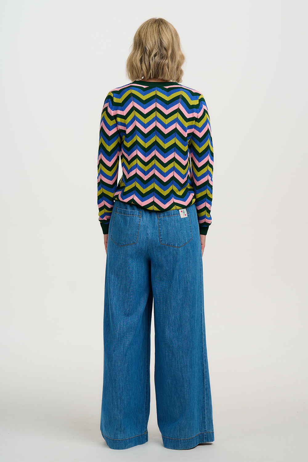 Woman wearing a colourful chevron-patterned sweater and blue jeans on a white background