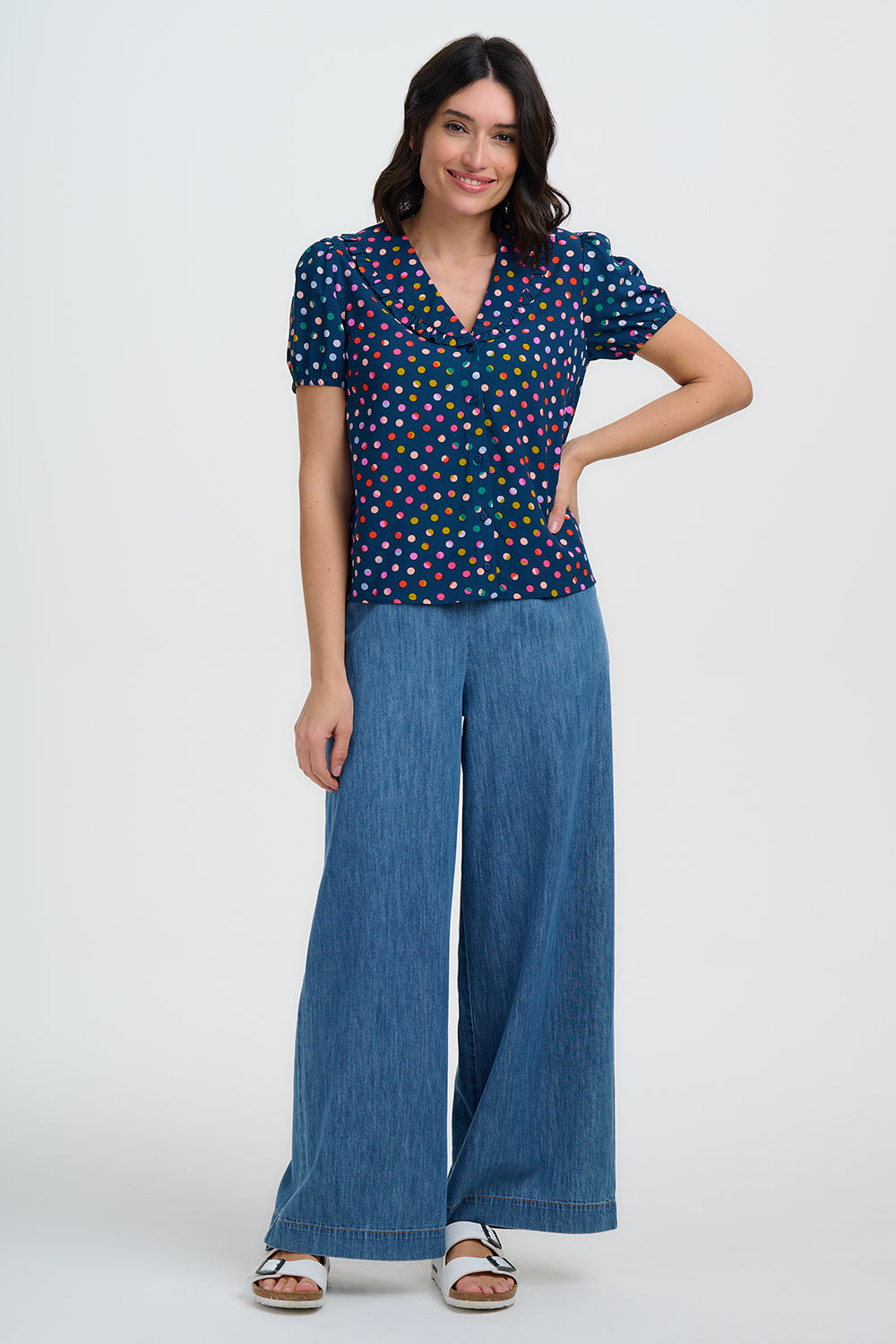 Woman wearing a navy polka dot top and wide-leg blue pants on a white background