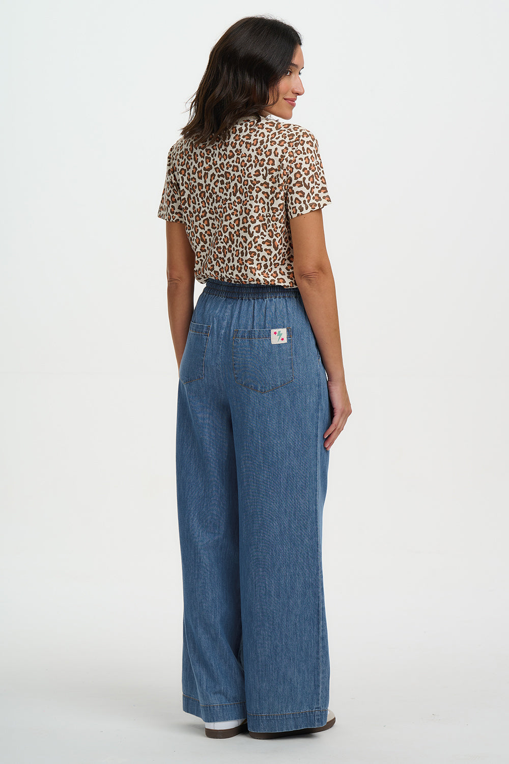 Woman wearing a leopard print top and blue denim pants on a white background