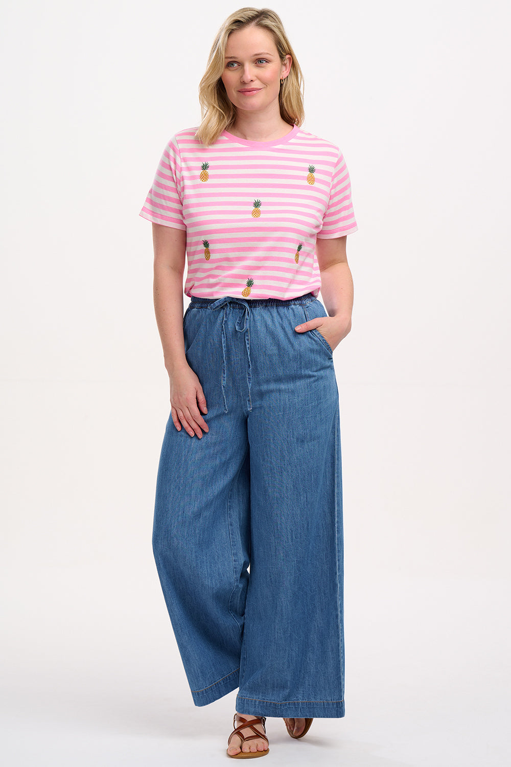 A model wearing mid blue denim wide leg trousers with an elasticated drawstring waist and back patch pockets.