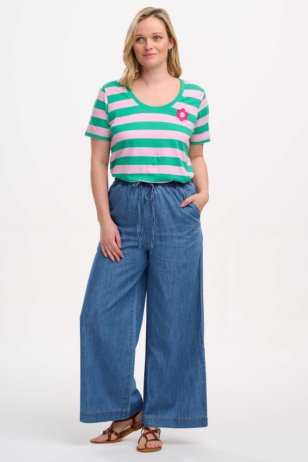 A model wearing mid blue denim wide leg trousers with an elasticated drawstring waist and back patch pockets.