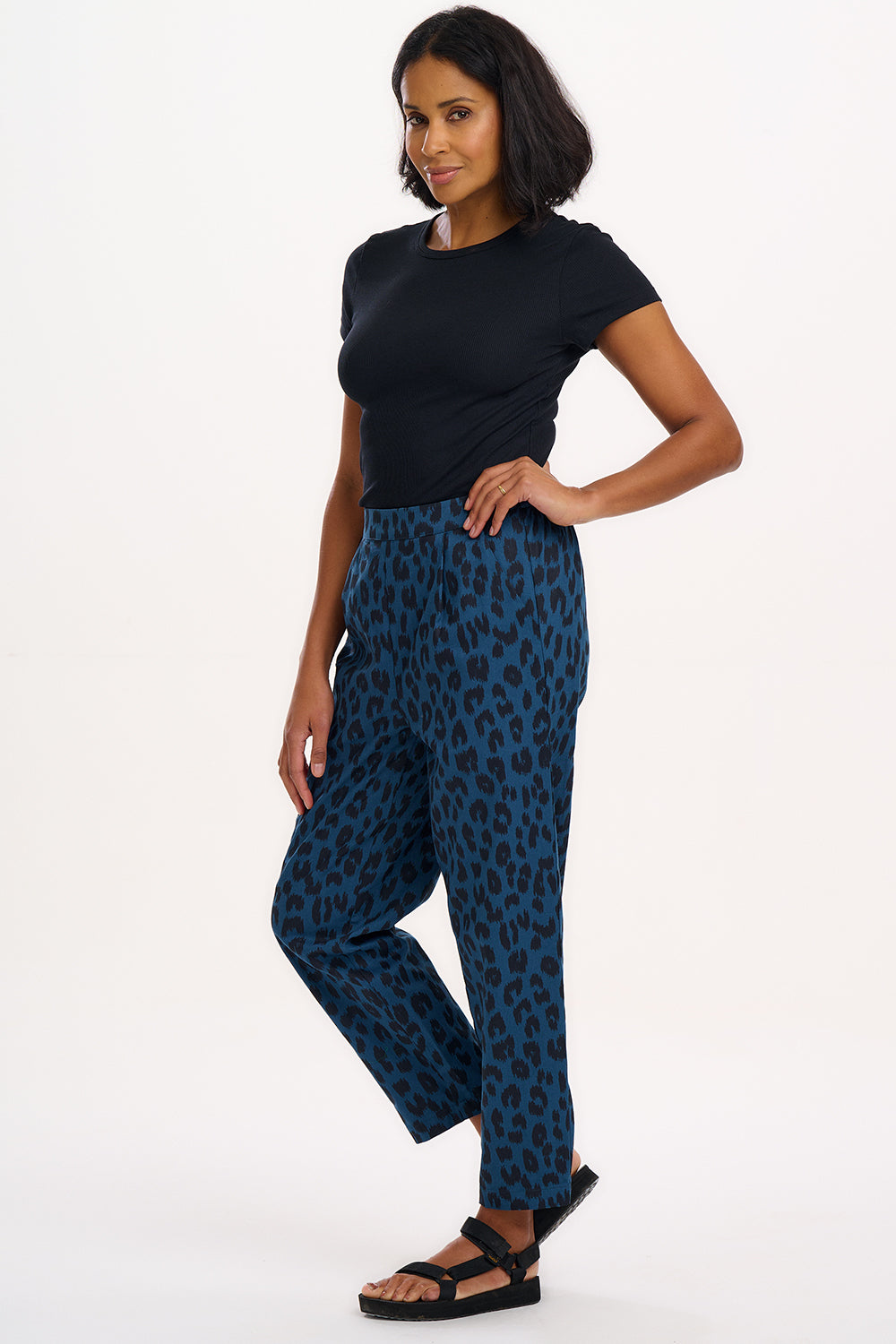 A woman modeling Romney trousers with a petrol navy color and a leopard print design.