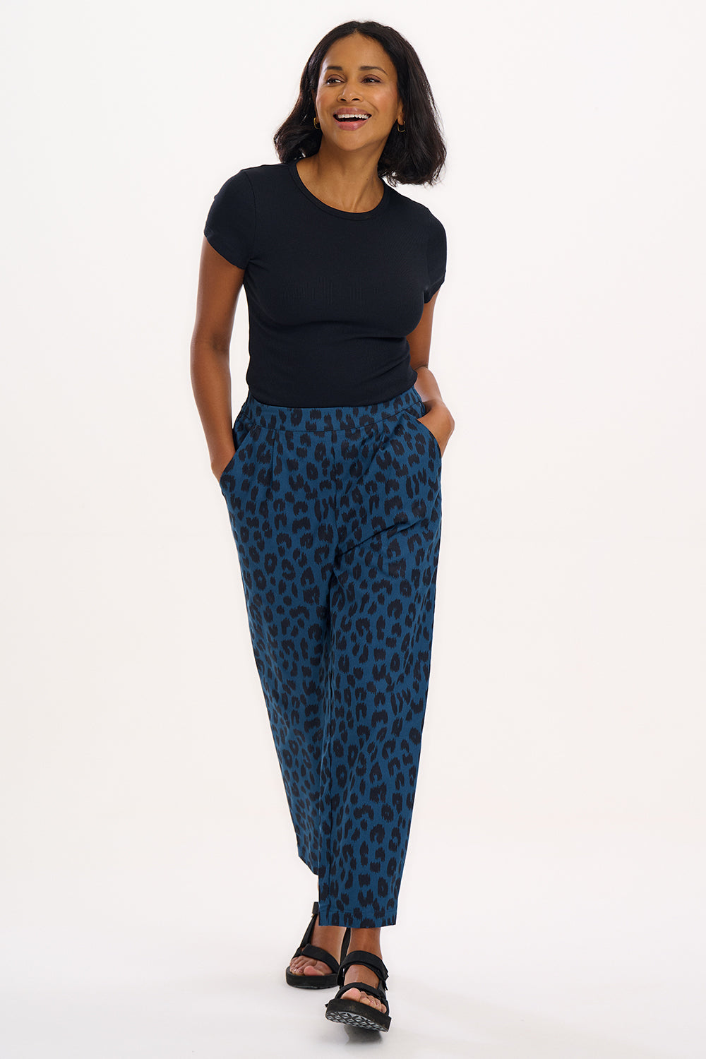 A woman modeling Romney trousers with a petrol navy color and a leopard print design.