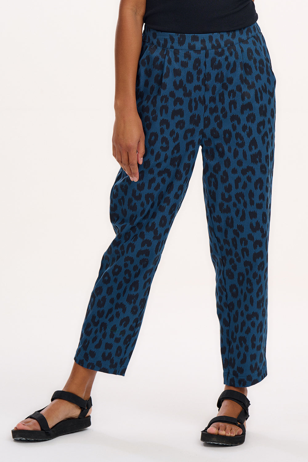 A woman modeling Romney trousers with a petrol navy color and a leopard print design.