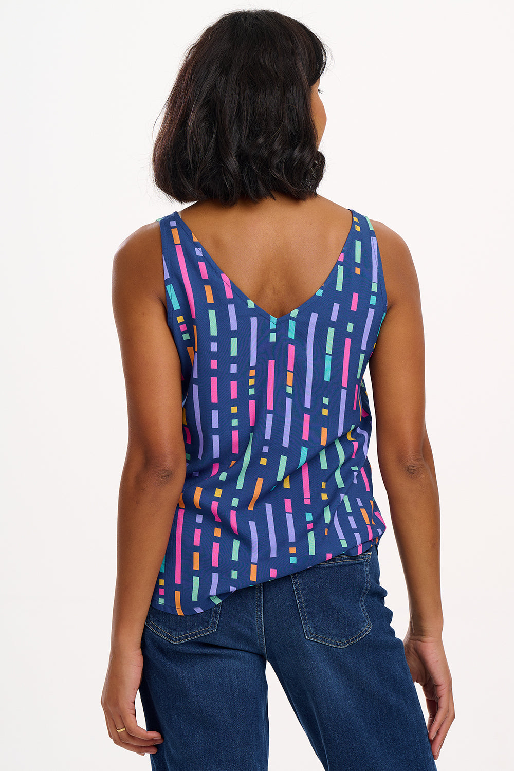 A model wearing a sleeveless blue vest top with a geometric pattern of broken lines in shades of purple, pink, green, and orange.