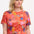 A woman wearing a red crew neck t-shirt with a painted jungle print, featuring vibrant colors and tropical motifs.