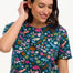 A woman smiling and wearing a teal t-shirt with a floral and dinosaur pattern, paired with a denim skirt.