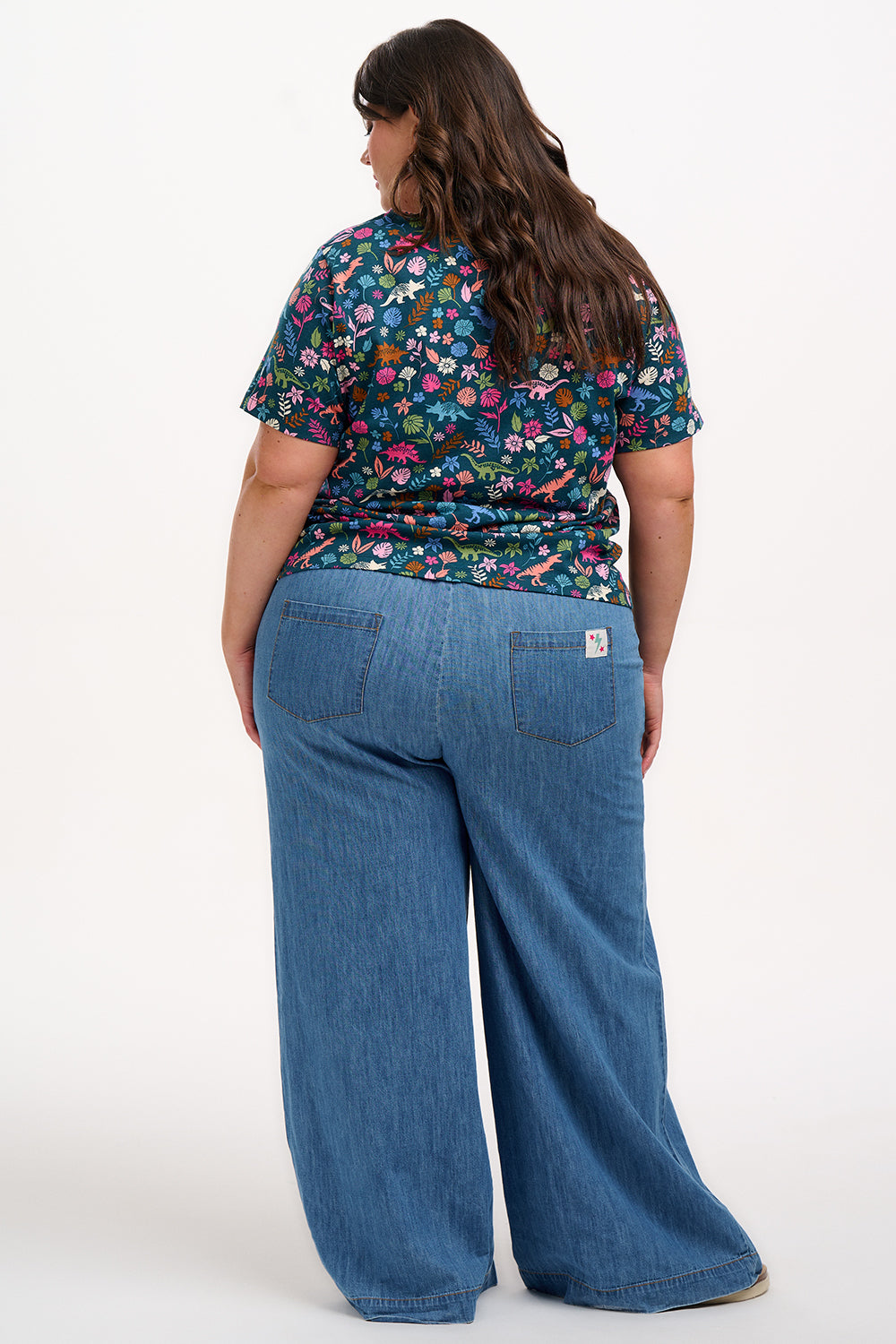 A woman smiling and wearing a teal t-shirt with a floral and dinosaur pattern, paired with a denim skirt.