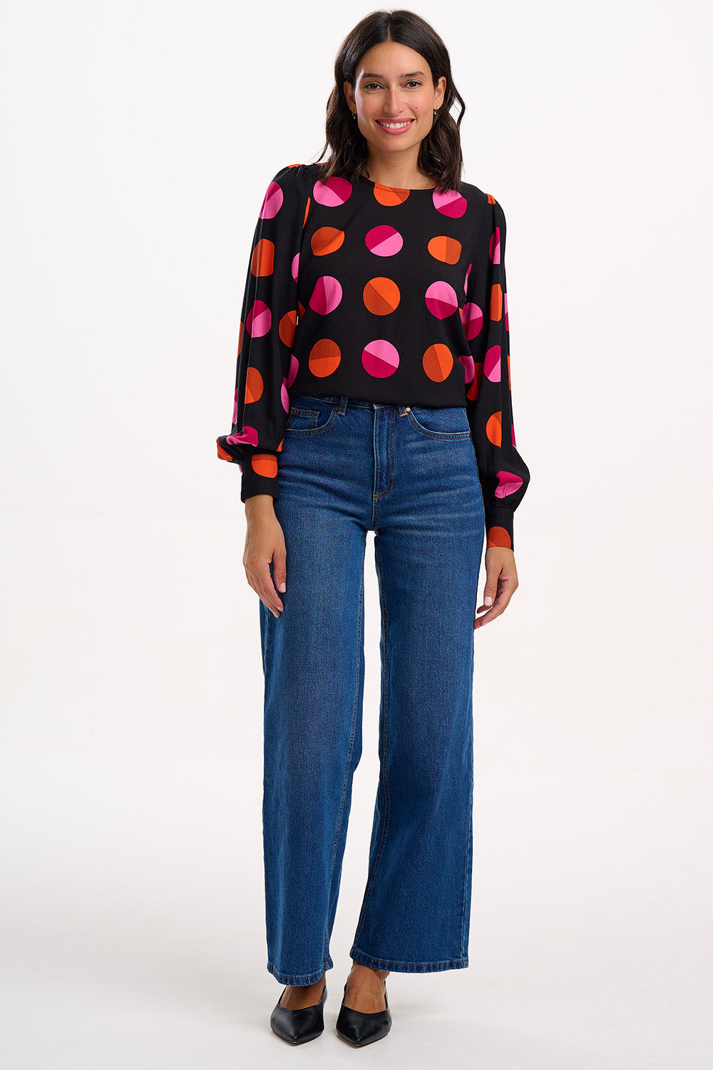 Woman wearing a black sweater with colorful polka dots and blue jeans on a white background