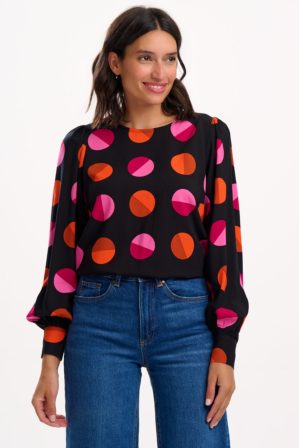 Woman wearing a black sweater with colorful polka dot pattern and blue jeans on a white background