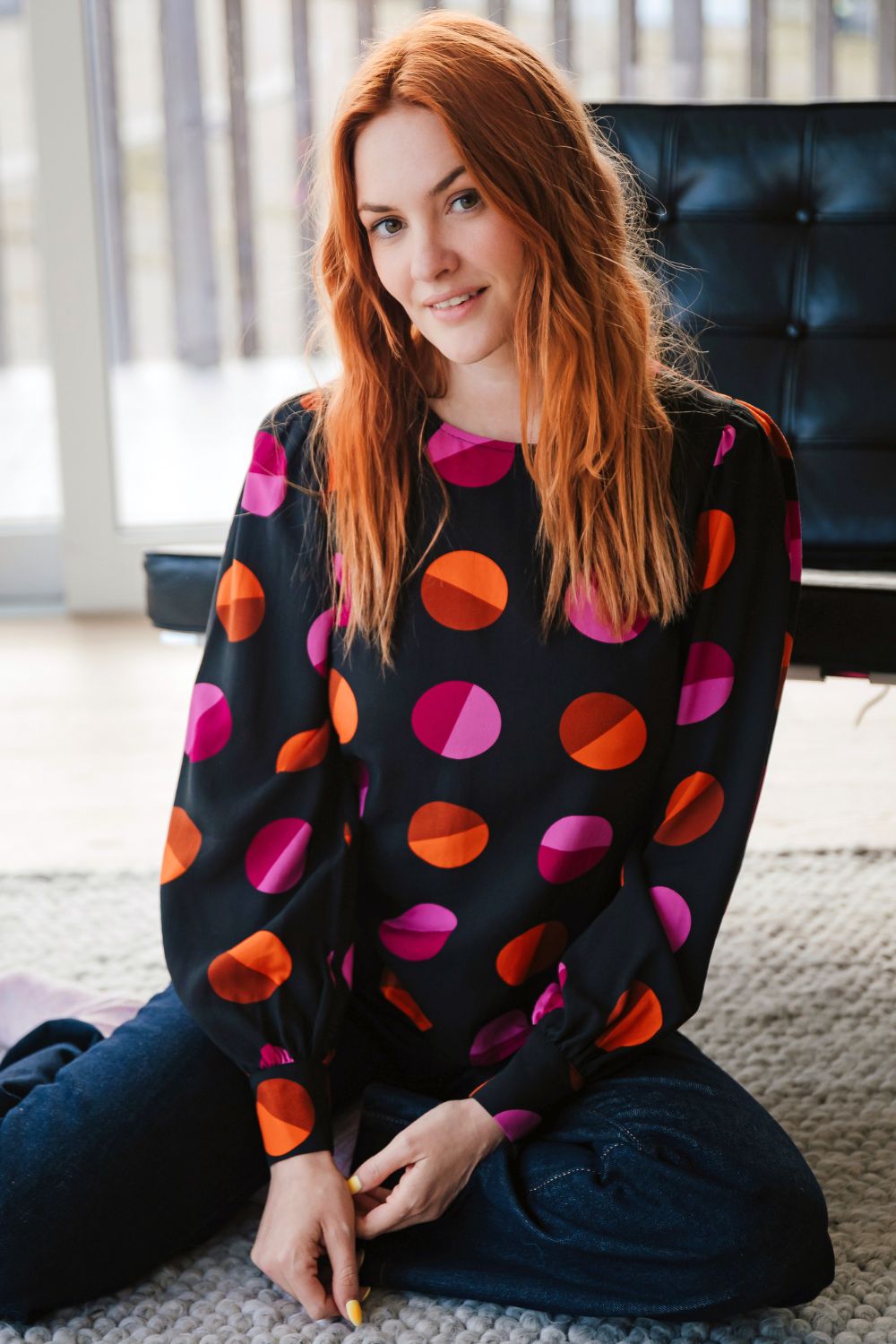 Woman wearing a colorful polka dot sweater sitting on the floor.