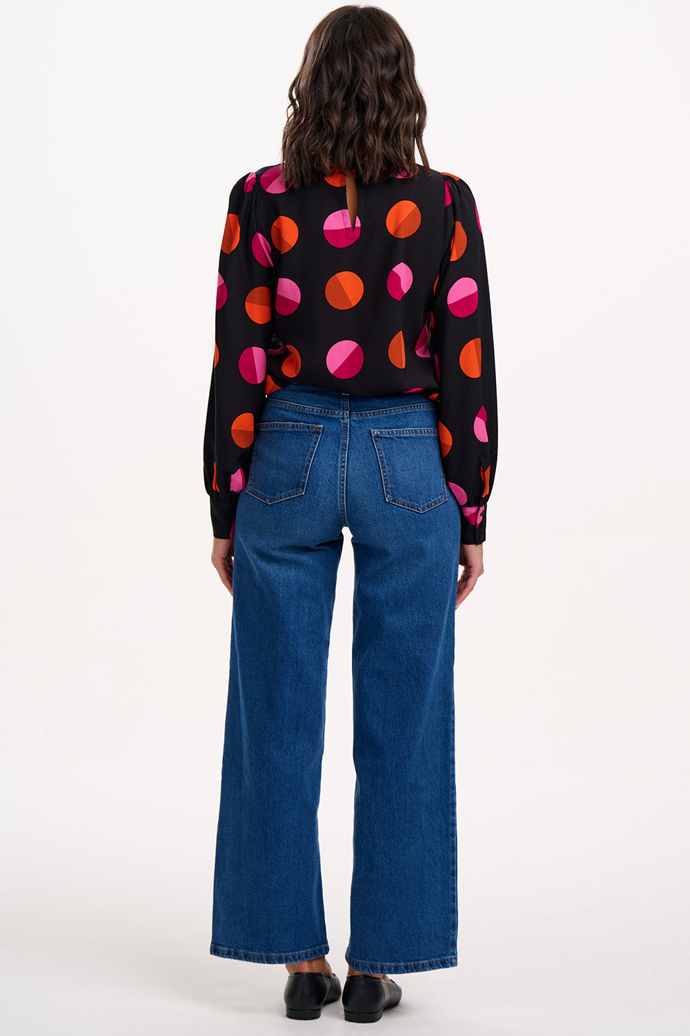 Person wearing a black sweater with colorful polka dots and blue jeans on a white background