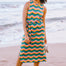 A woman standing on the beach wearing a sleeveless, midi-length, multicolored jersey dress with a pattern of rainbow waves in shades of pink, green, blue, and tan.