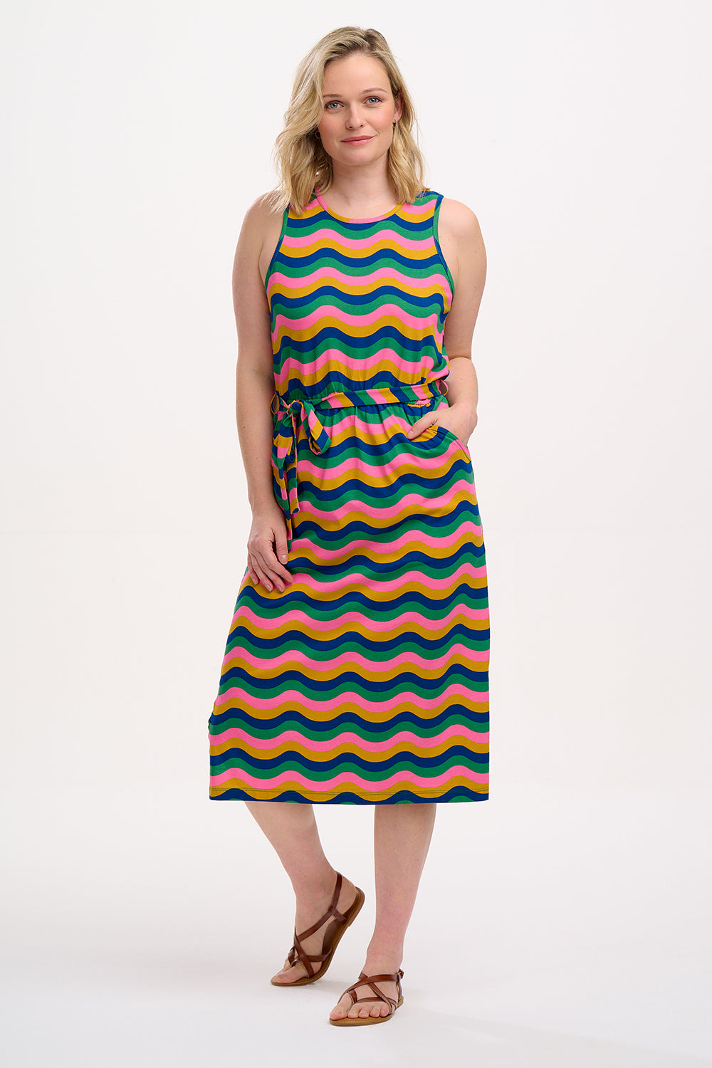 A model wearing a sleeveless, midi-length multicolor jersey dress with a wave pattern in shades of pink, green, blue, and tan.