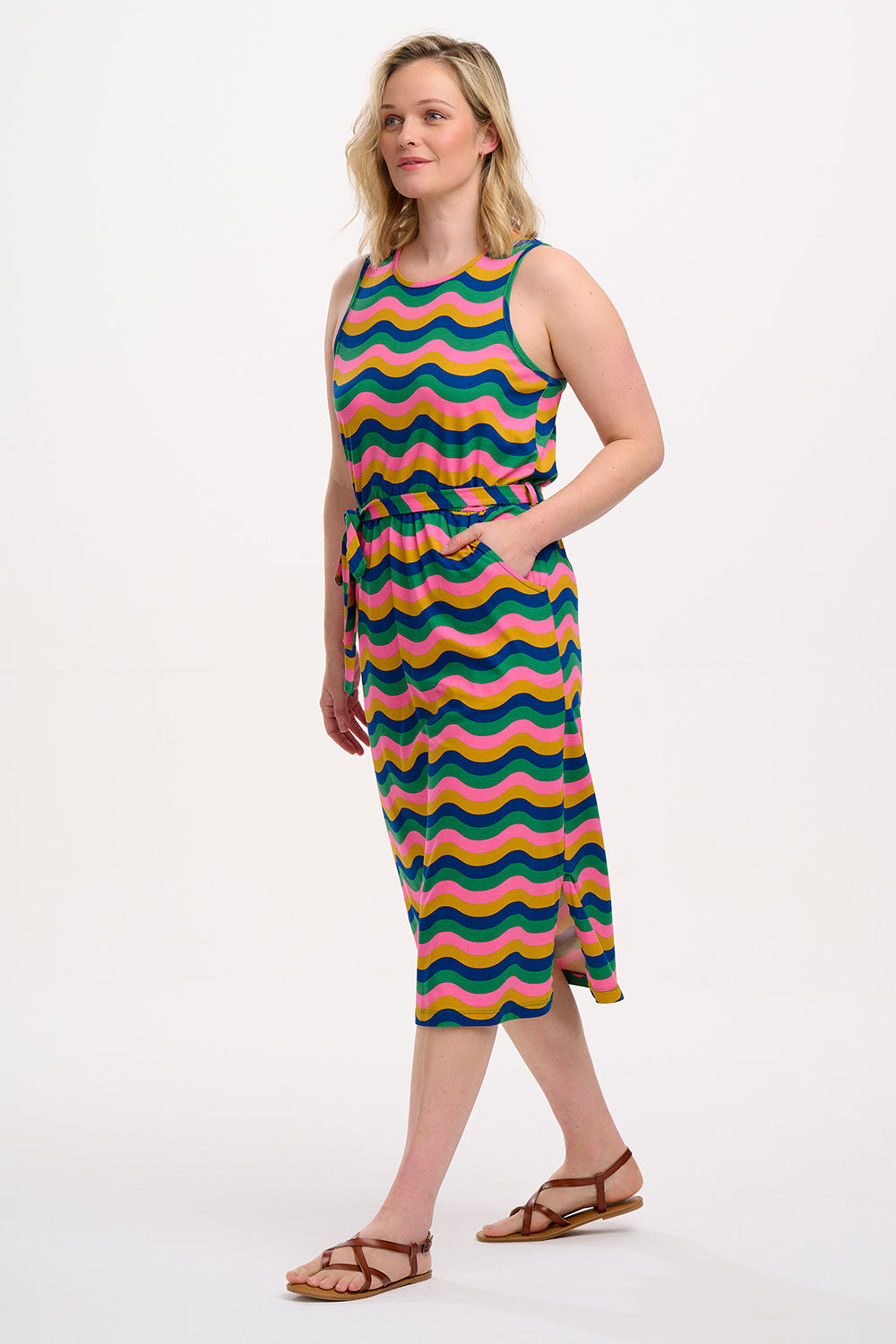 A model wearing a sleeveless, midi-length multicolor jersey dress with a wave pattern in shades of pink, green, blue, and tan.