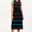 A model wearing a sleeveless, striped midi dress in black with bands of pink, green, blue, and orange. She is also wearing pink strappy sandals.