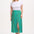 A woman standing, wearing a white top and the Rosalind Skirt in green with a rainbow pebbles print.