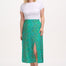 A woman standing, wearing a white top and the Rosalind Skirt in green with a rainbow pebbles print.