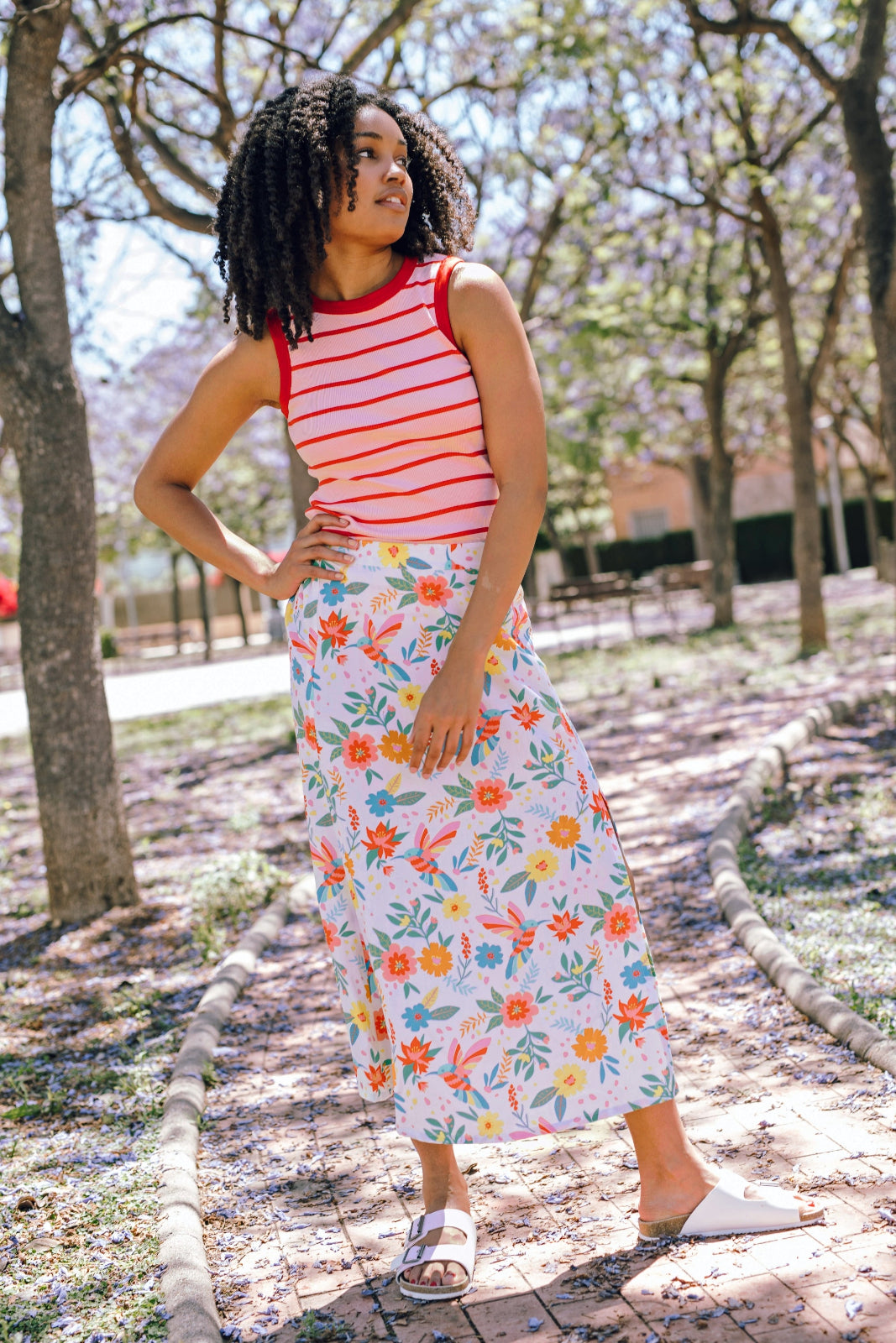 A woman wearing an off-white skirt with a tropical hummingbird print, paired with a red and white striped top.