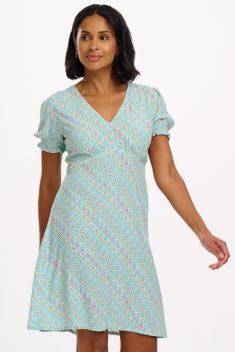 A woman wearing a short off-white mini tea dress with a multicolor floral garden waves pattern, featuring short shirred sleeves.