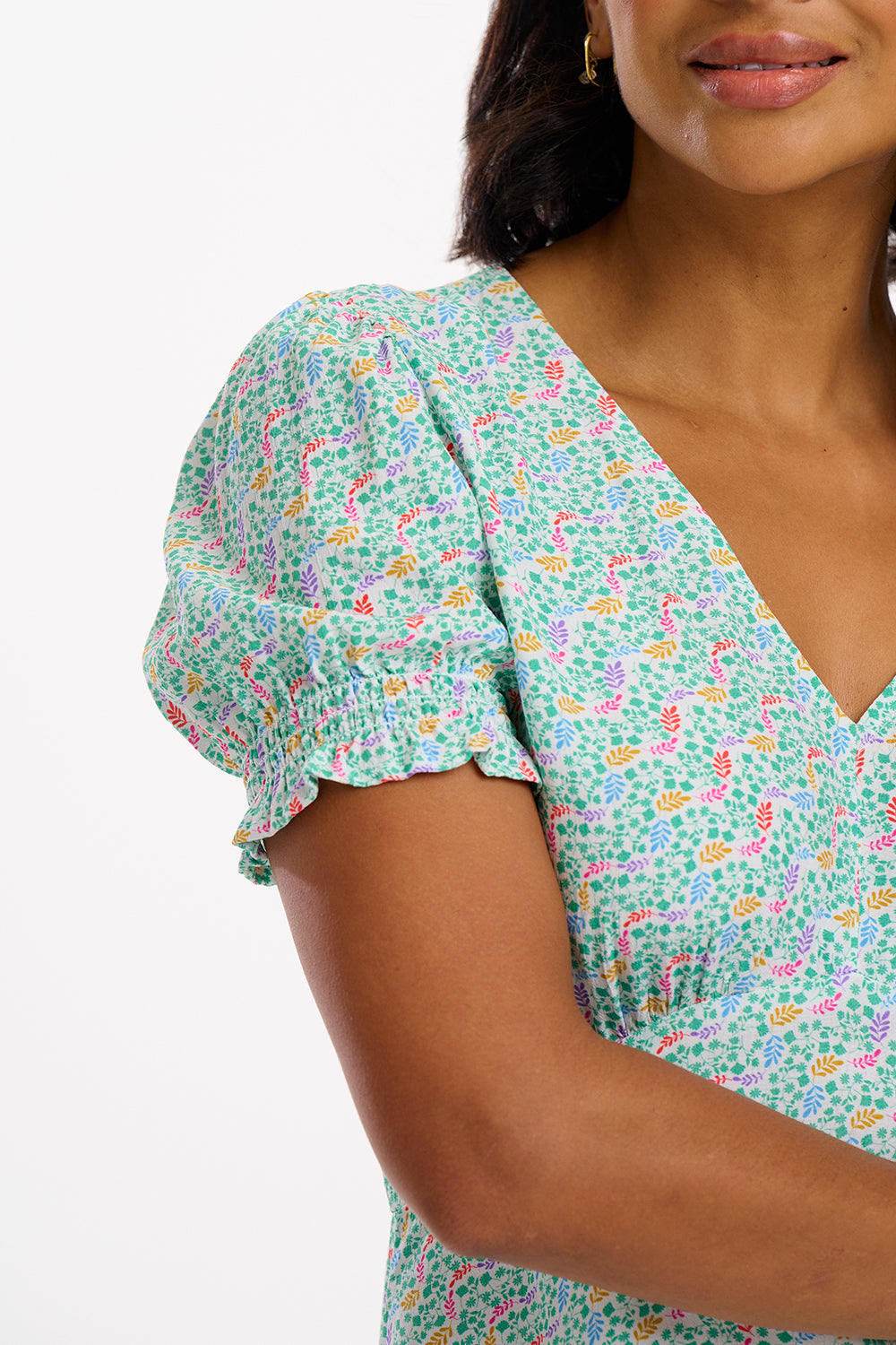 A woman wearing a short off-white mini tea dress with a multicolor floral garden waves pattern, featuring short shirred sleeves.