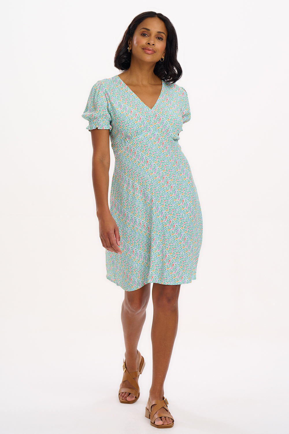 A woman wearing a short off-white mini tea dress with a multicolor floral garden waves pattern, featuring short shirred sleeves.