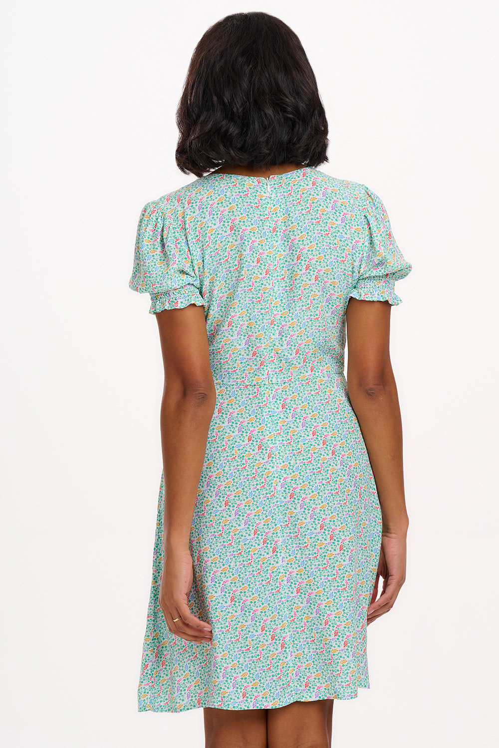 A woman wearing a short off-white mini tea dress with a multicolor floral garden waves pattern, featuring short shirred sleeves.
