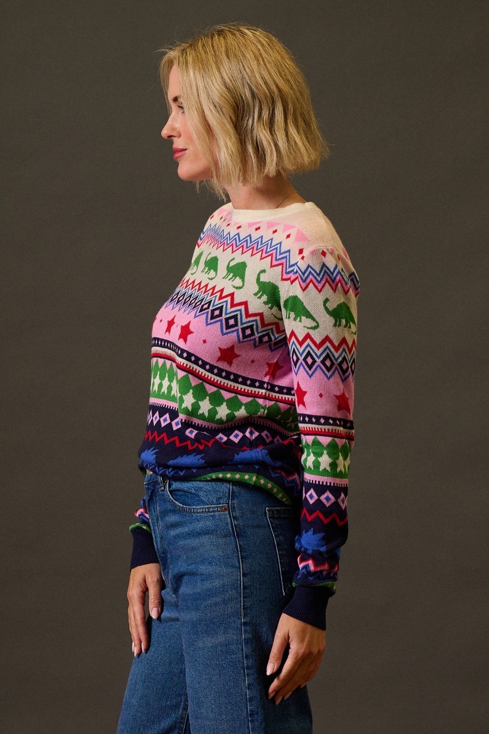 Woman wearing a colorful patterned sweater and blue jeans against a brown background