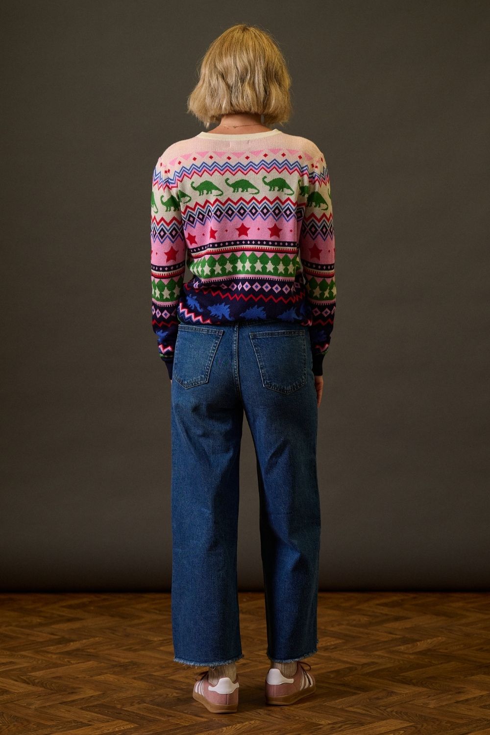 Person wearing a colorful patterned sweater and blue jeans standing against a plain background