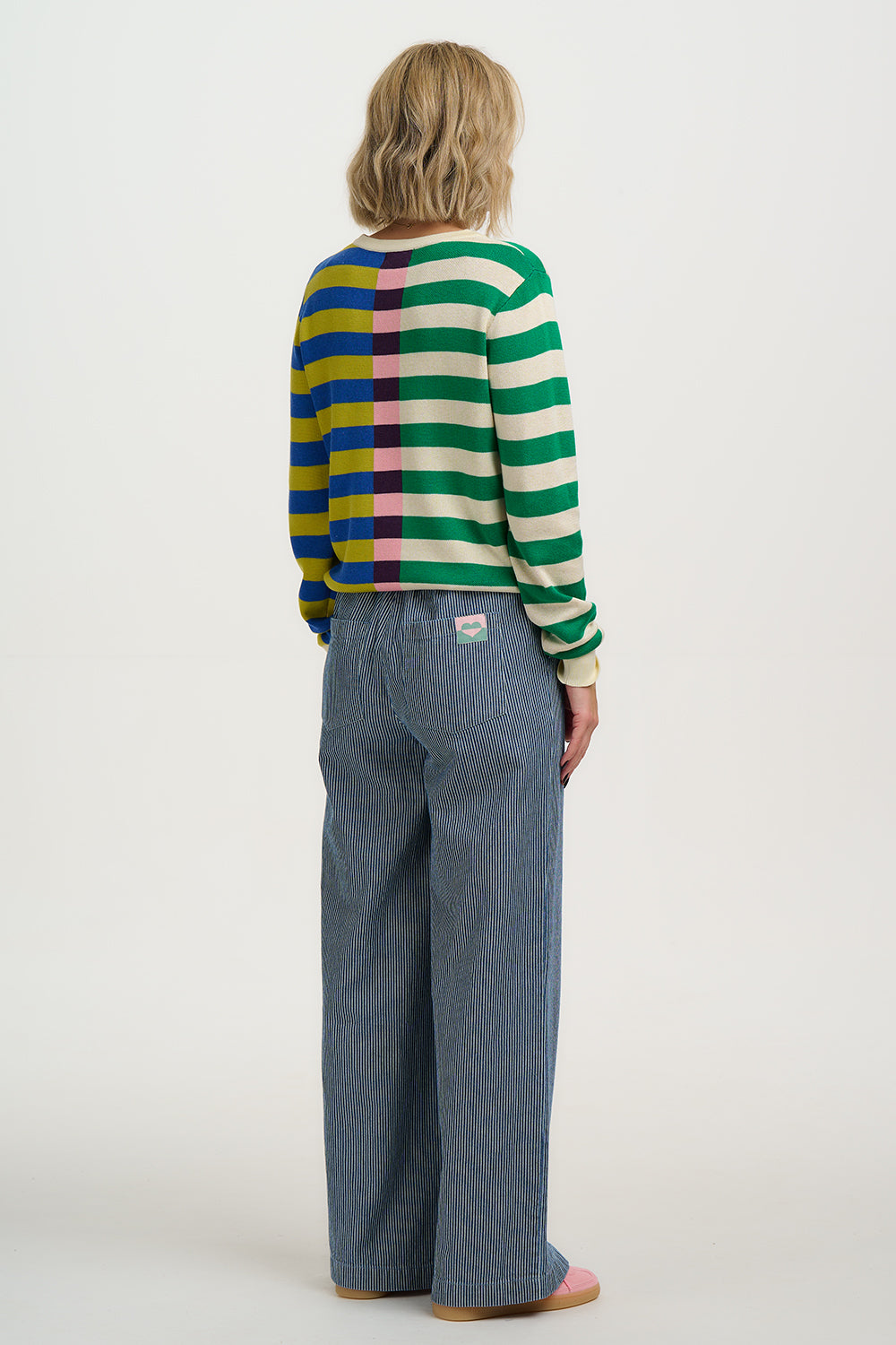 Person wearing a colorful striped sweater and blue jeans on a white background