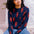 A person sitting on the ground wearing a navy crew neck jumper with a bold lobster repeat pattern in red.
