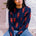 A person sitting on the ground wearing a navy crew neck jumper with a bold lobster repeat pattern in red.