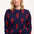 A person wearing a navy crew neck jumper with a bold lobster repeat pattern in red.