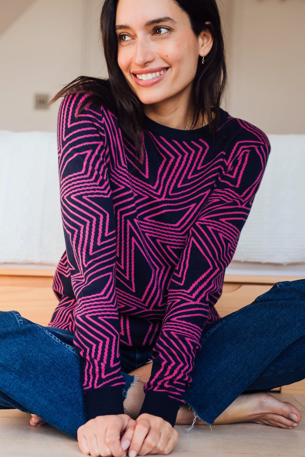 A woman sitting on the floor, wearing a navy crew neck jumper with a pink star explosion pattern.