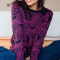 A woman sitting on the floor, wearing a navy crew neck jumper with a pink star explosion pattern.