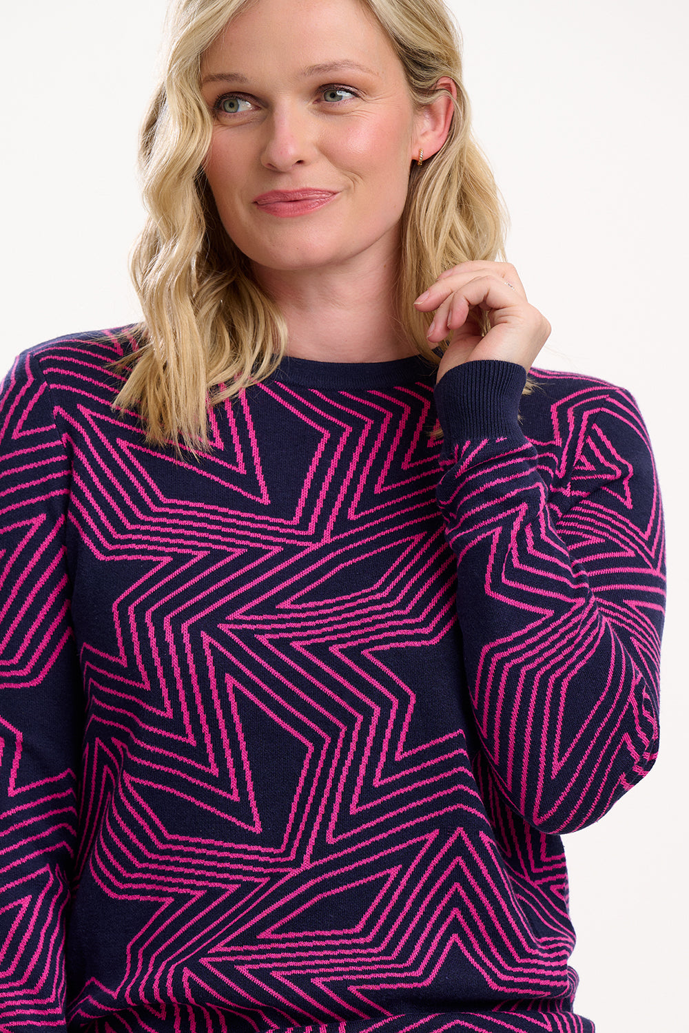 Woman wearing a navy sweater with pink geometric pattern on a white background