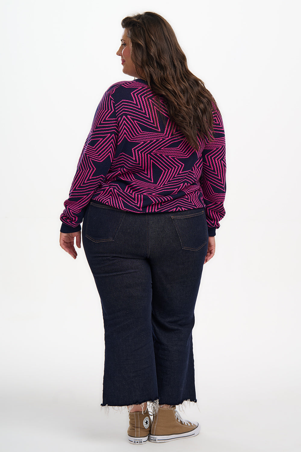 Person wearing a purple patterned top and dark pants on a white background