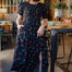 A woman smiling and posing in a midi dress with a black and rainbow polka dot print, featuring a shirred bodice and elasticated puff sleeves.