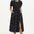 A model wearing a black midi dress with a rainbow sprigs print, featuring colorful ditsy flowers and stars, with a shirred bodice, elasticated puff sleeves, and a split hem.