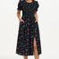 A model wearing a black midi dress with a rainbow sprigs print, featuring colorful ditsy flowers and stars, with a shirred bodice, elasticated puff sleeves, and a split hem.