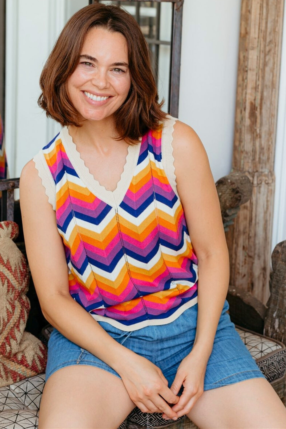 Woman wearing a colorful zigzag patterned top and denim shorts sitting on a couch.