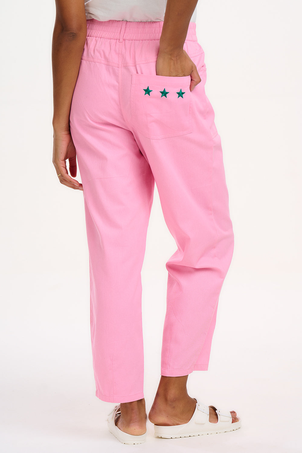 A model wearing pink Rowan trousers with a triple star pattern, paired with a striped top, standing against a white background.